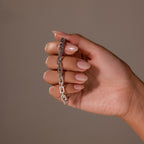 A hand with manicured nails displays the Eternal Link Bracelet in Silver, a modern accessory with a sleek geometric design, set against a plain beige background.