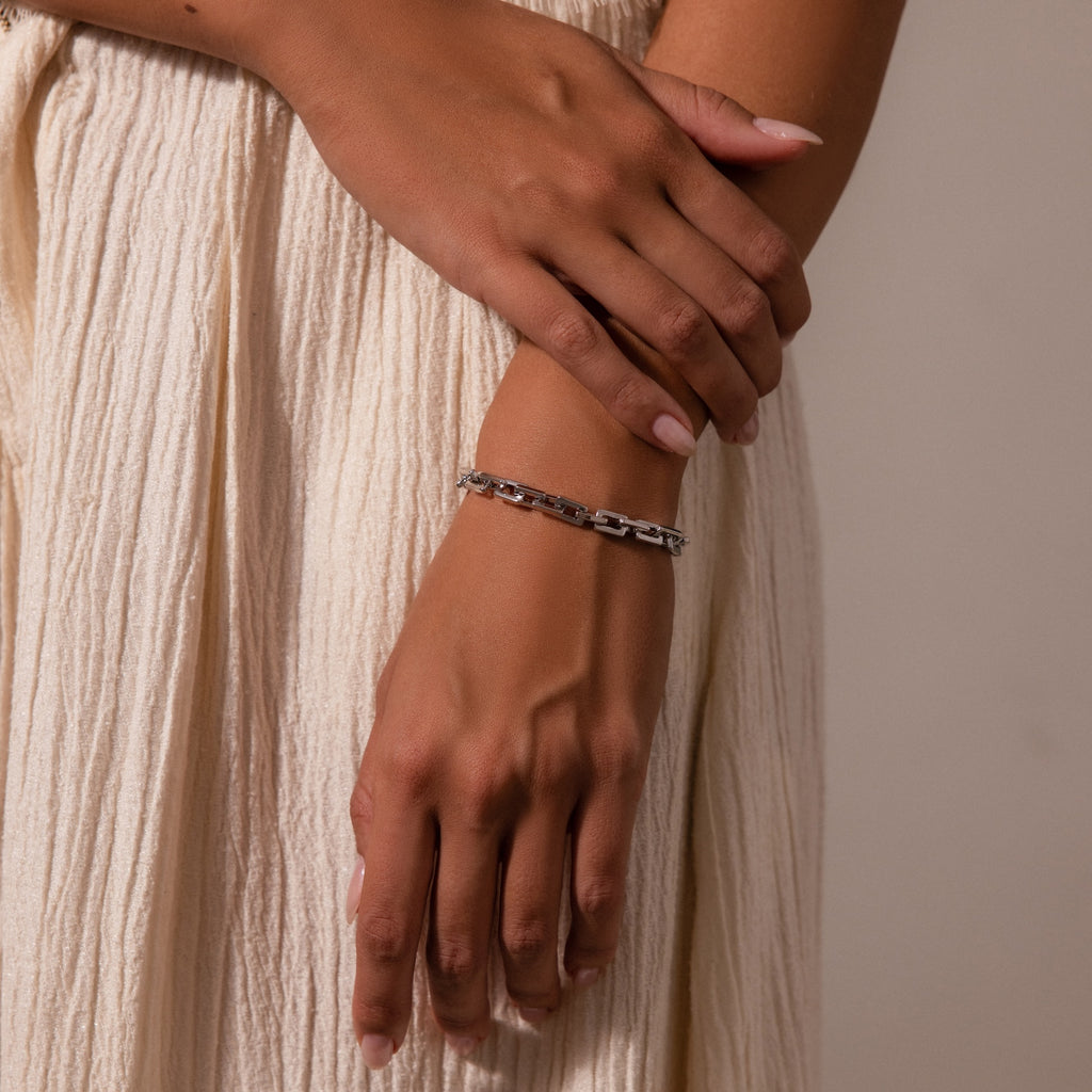 A person wearing the Eternal Link Bracelet in Silver with a geometric design and a cream pleated skirt, hands gently crossed—a perfect touch of modern essentials.