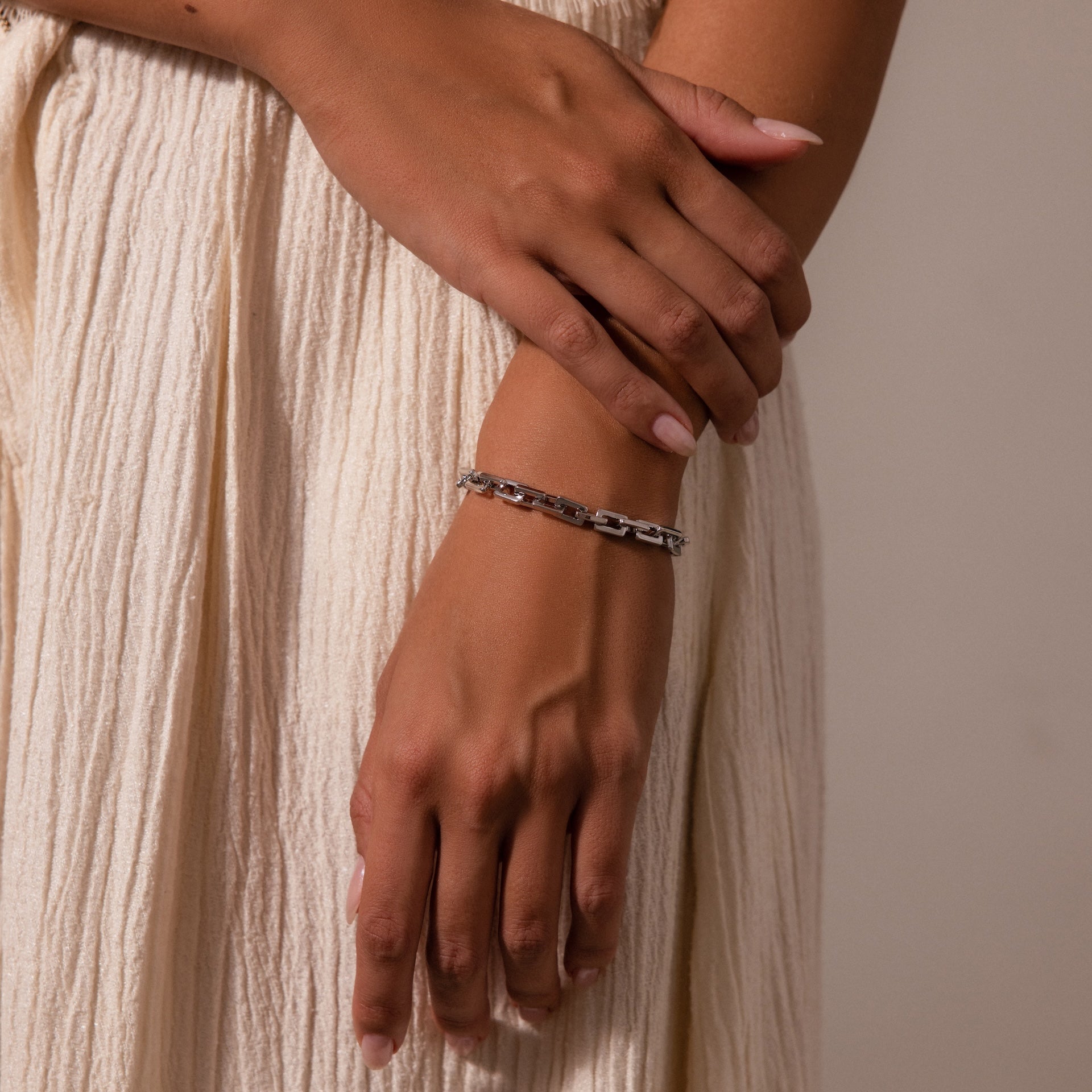 A person wearing the Eternal Link Bracelet, a modern essential with a geometric design, gently crosses their hands while dressed in a cream pleated skirt.
