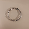 The Eternal Link Bracelet in Silver features rectangular links in a circle on a beige background, highlighting its geometric, modern design.