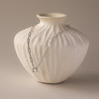 The Paperclip Clasp Necklace in White Gold is elegantly draped over a textured white ceramic vase against a neutral background.