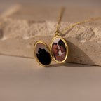 A Floral Handwriting Locket Necklace opens to reveal two couple photos, resting on a stone surface.