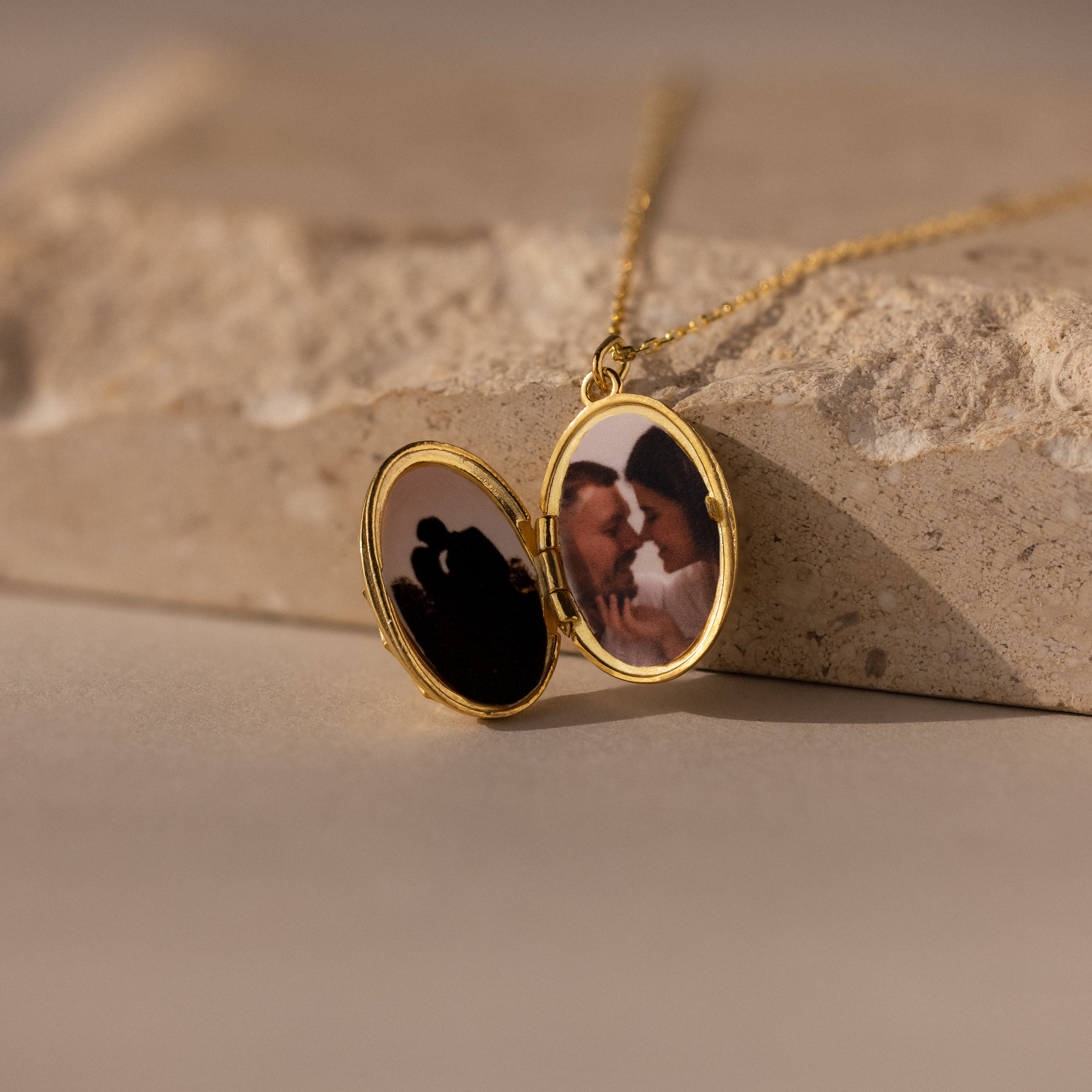 A Floral Handwriting Locket Necklace opens to reveal two couple photos, resting on a stone surface.