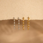The Diamond Chain Drop Earrings in 18K Gold are displayed on a textured beige surface, highlighting their elegant design.