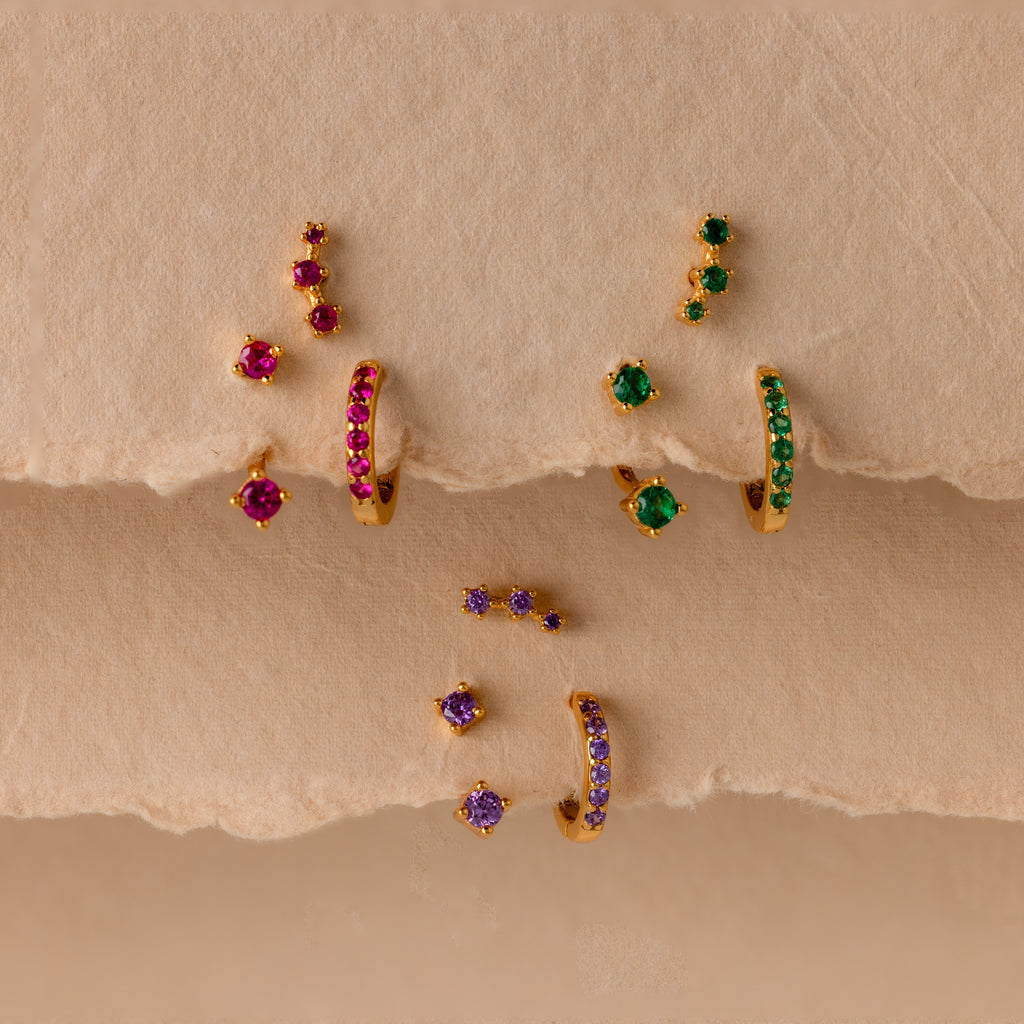 Ruby Earring Trio Set featuring gold earrings with red, green, and purple gemstones displayed on textured beige paper.