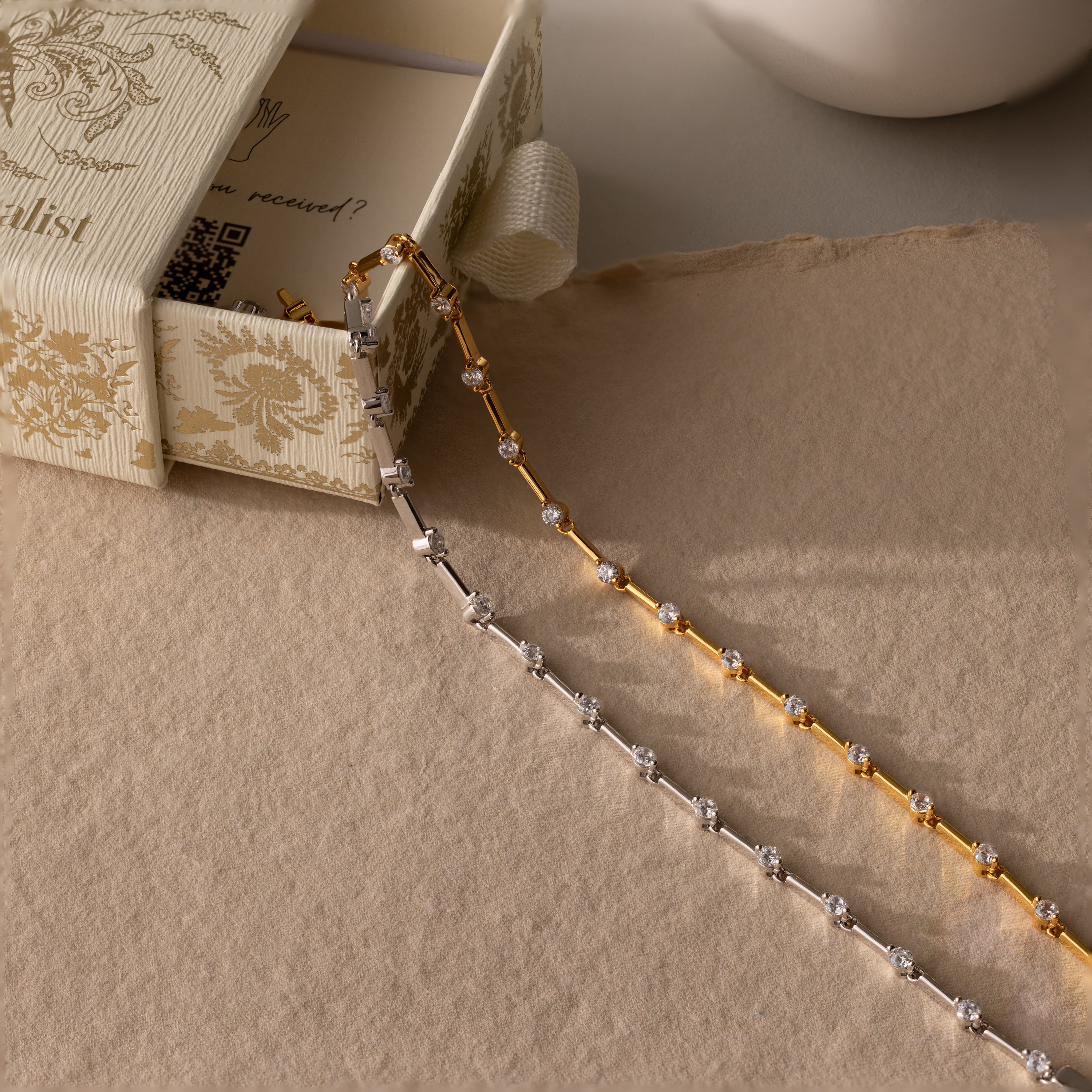Two delicate chain necklaces, one gold and one silver with small gemstones, displayed on a textured surface—perfect for pairing with the Sprinkle Diamond Tennis Bracelet.