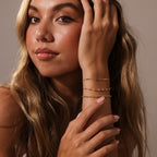 A woman with long blonde hair wears layered bracelets, including the Sprinkle Diamond Tennis Bracelet, resting her hand on her face and looking at the camera.