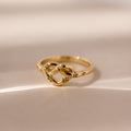 The Starry Love Knot Ring, featuring a delicate gold band with an intricate love knot design, rests on a soft beige surface—symbolizing timeless elegance and heartfelt connection.