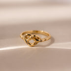 The Starry Love Knot Ring, featuring a delicate gold band with an intricate love knot design, rests on a soft beige surface—symbolizing timeless elegance and heartfelt connection.