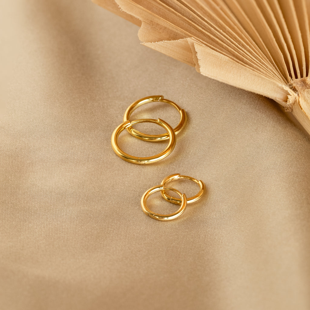 Four Small Bold Hoops with a minimalist design rest on beige fabric beside an open book, making them perfect for everyday wear.