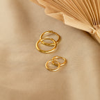 Four Small Bold Hoops with a minimalist design rest on beige fabric beside an open book, making them perfect for everyday wear.