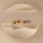 The Pink Baguette Opal Studs feature rectangular and round stones, beautifully arranged on a soft beige surface—an elegant, chic choice for bridal gifts.