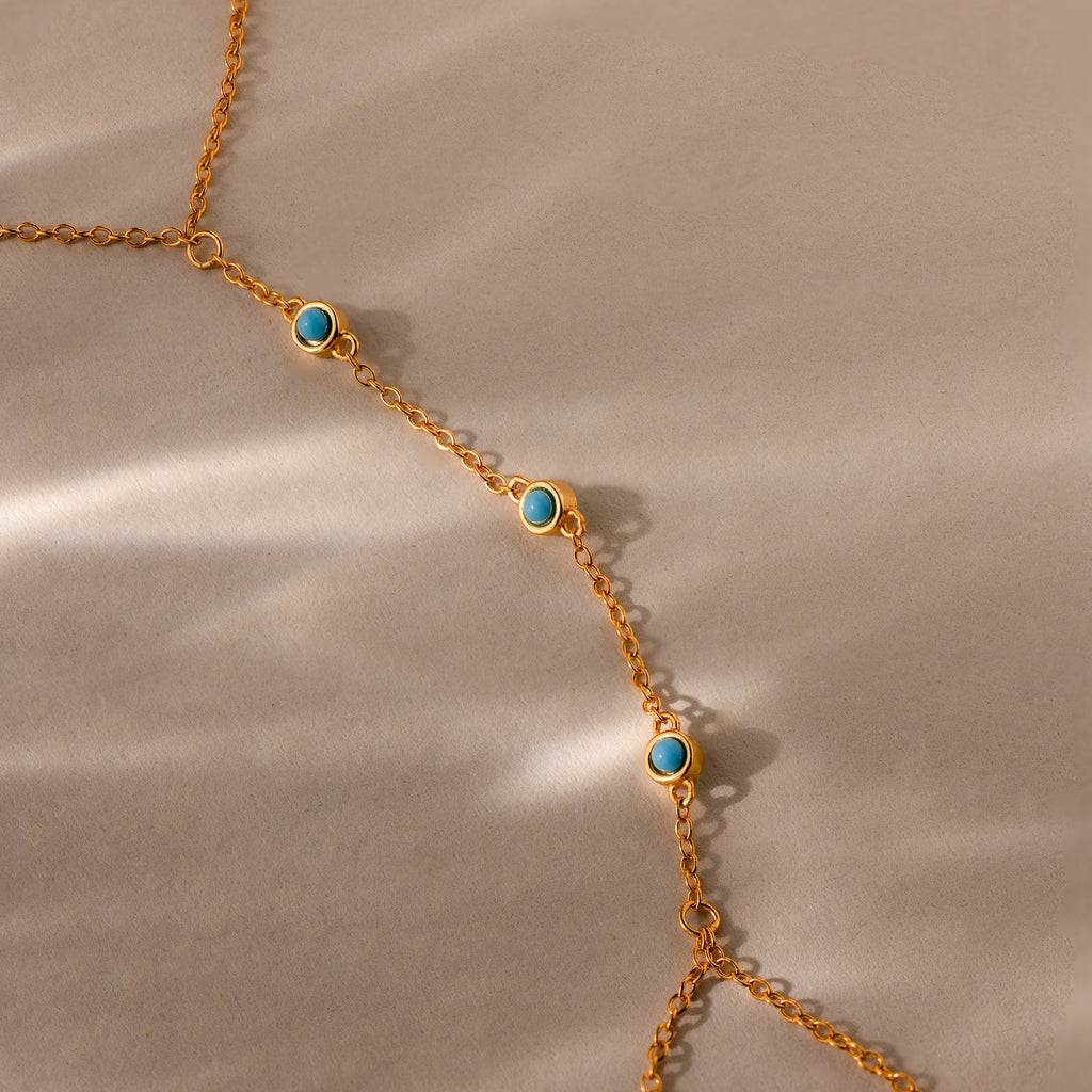 Turquoise Hand Chain Bracelet featuring a gold delicate chain with small turquoise stones, displayed diagonally on a beige background with soft shadows.