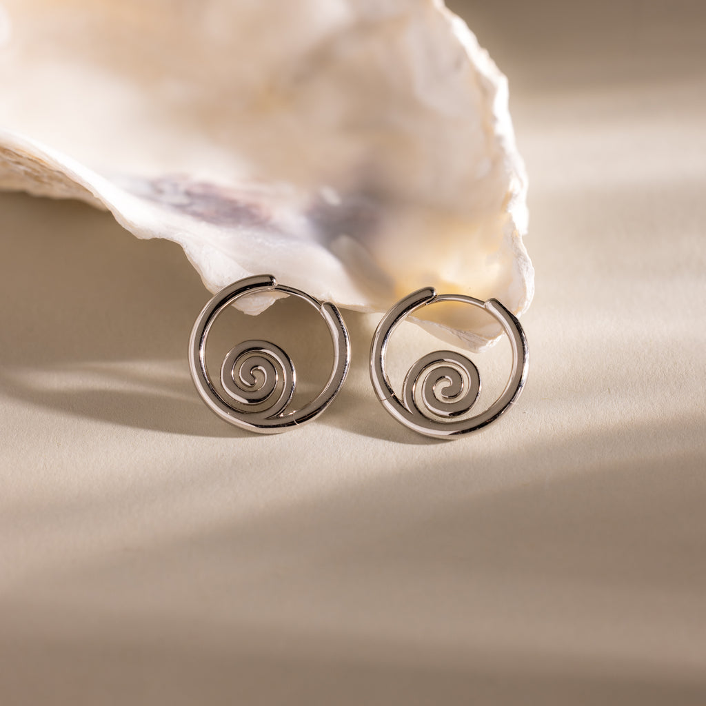 Spiral Swirl Hoops shown in front of a seashell on a beige surface with soft lighting—stylish earrings to enhance your boho vacation outfits.
