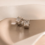 Two Pave Checkered Huggies in Silver with embedded gems, shown on a soft beige surface with white ribbon.