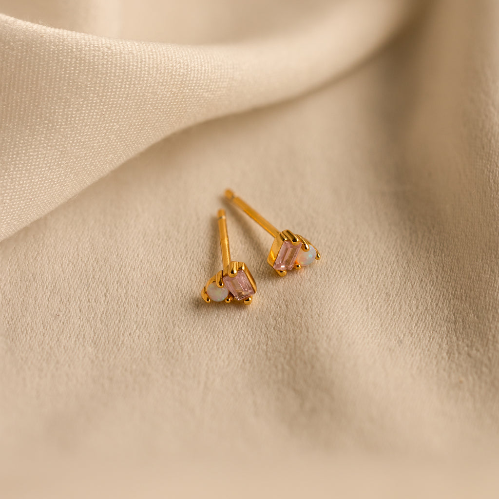 Pink Baguette Opal Studs with shimmering pink gemstones rest on soft beige fabric—ideal elegant bridal gifts.