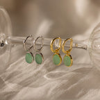 A pair of Jade Drop Hoops in Silver with green jade gemstone pendants is displayed on a glass stem.