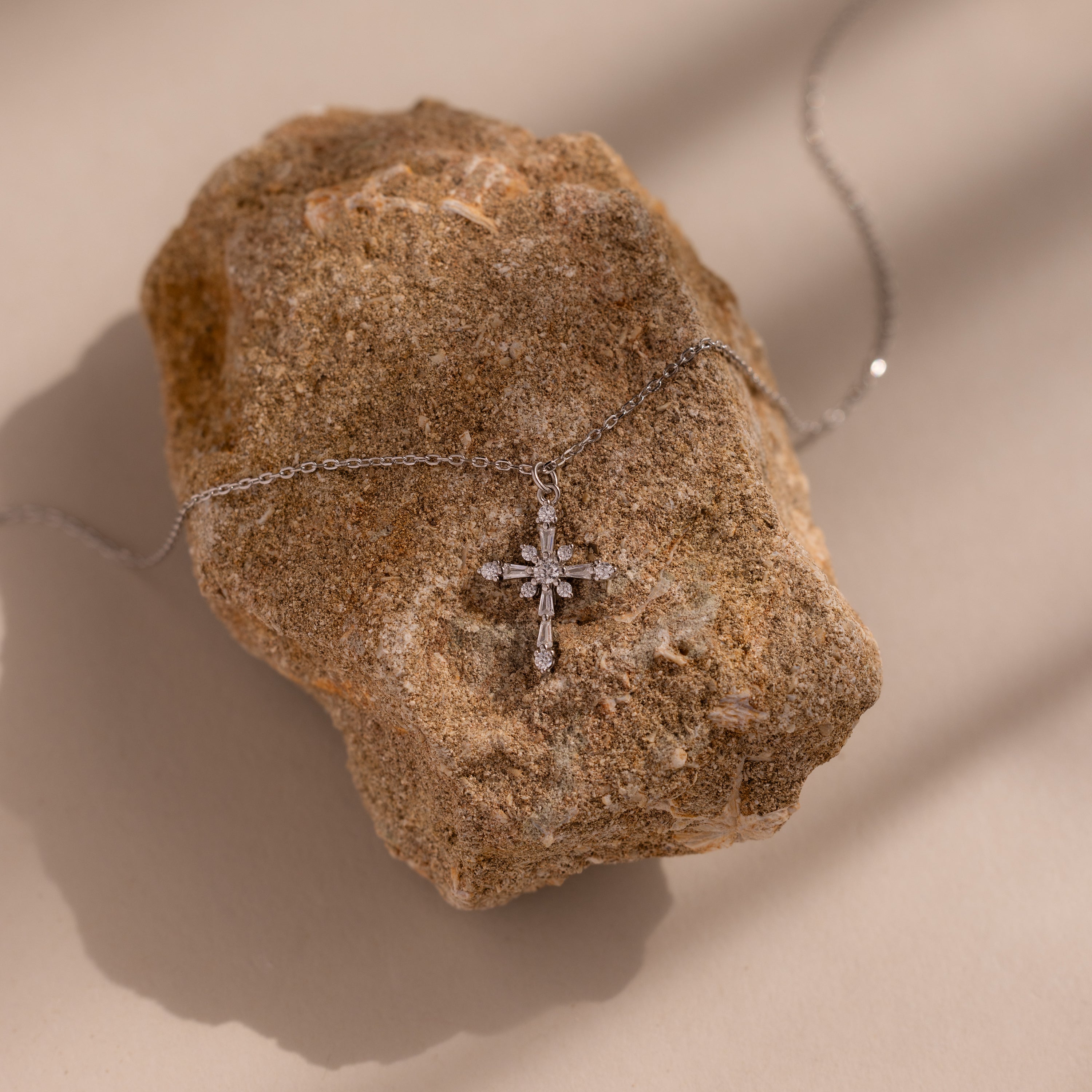 The Vintage Diamond Cross Necklace in Silver is displayed on a rough brown stone with soft shadows.