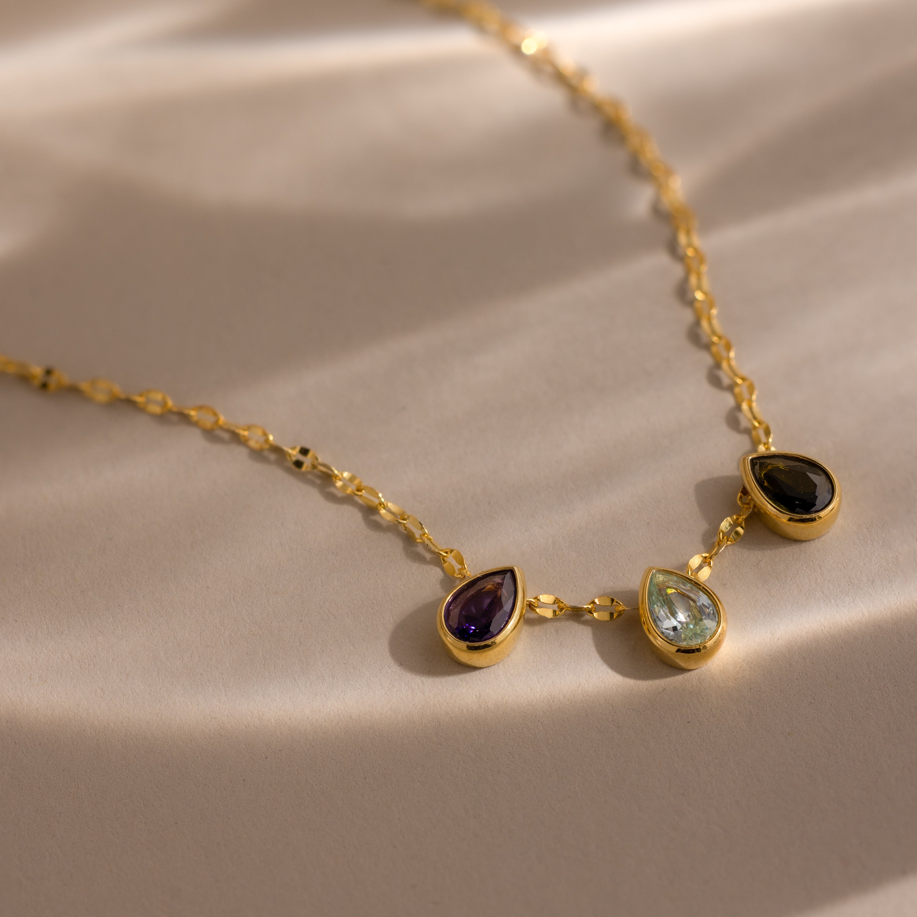 The Multiple Teardrop Birthstone Necklace features three gold-set teardrop gemstones on a chain, making it a meaningful gift for any occasion.
