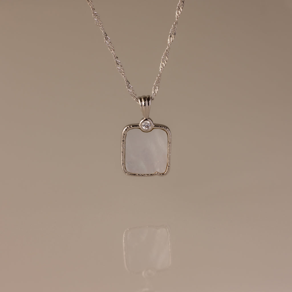 The Square Mother of Pearl Necklace in Silver features a shimmering iridescent pendant with a small round stone—ideal for layering on any plain background.
