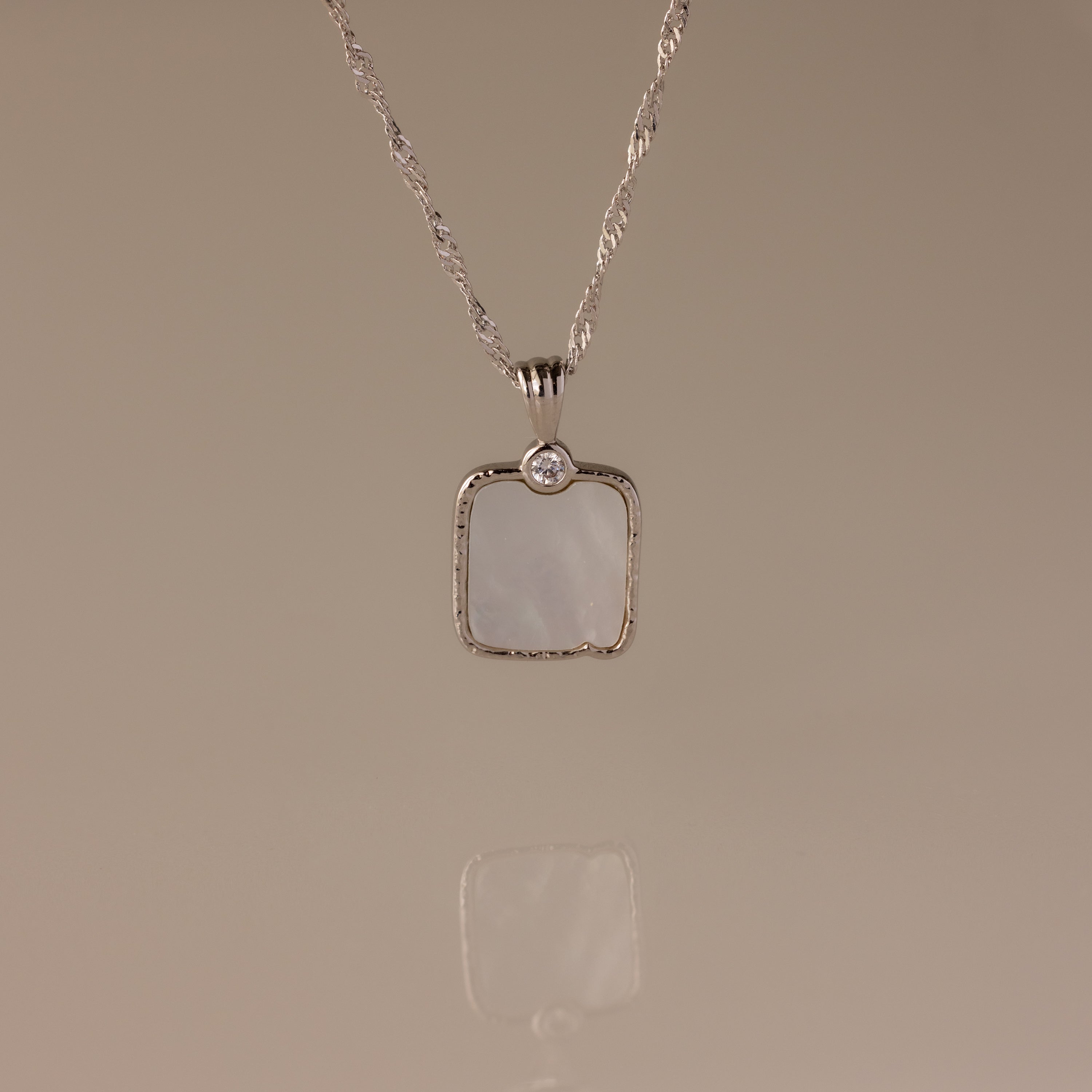 The Square Mother of Pearl Necklace in Silver features a shimmering iridescent pendant with a small round stone—ideal for layering on any plain background.
