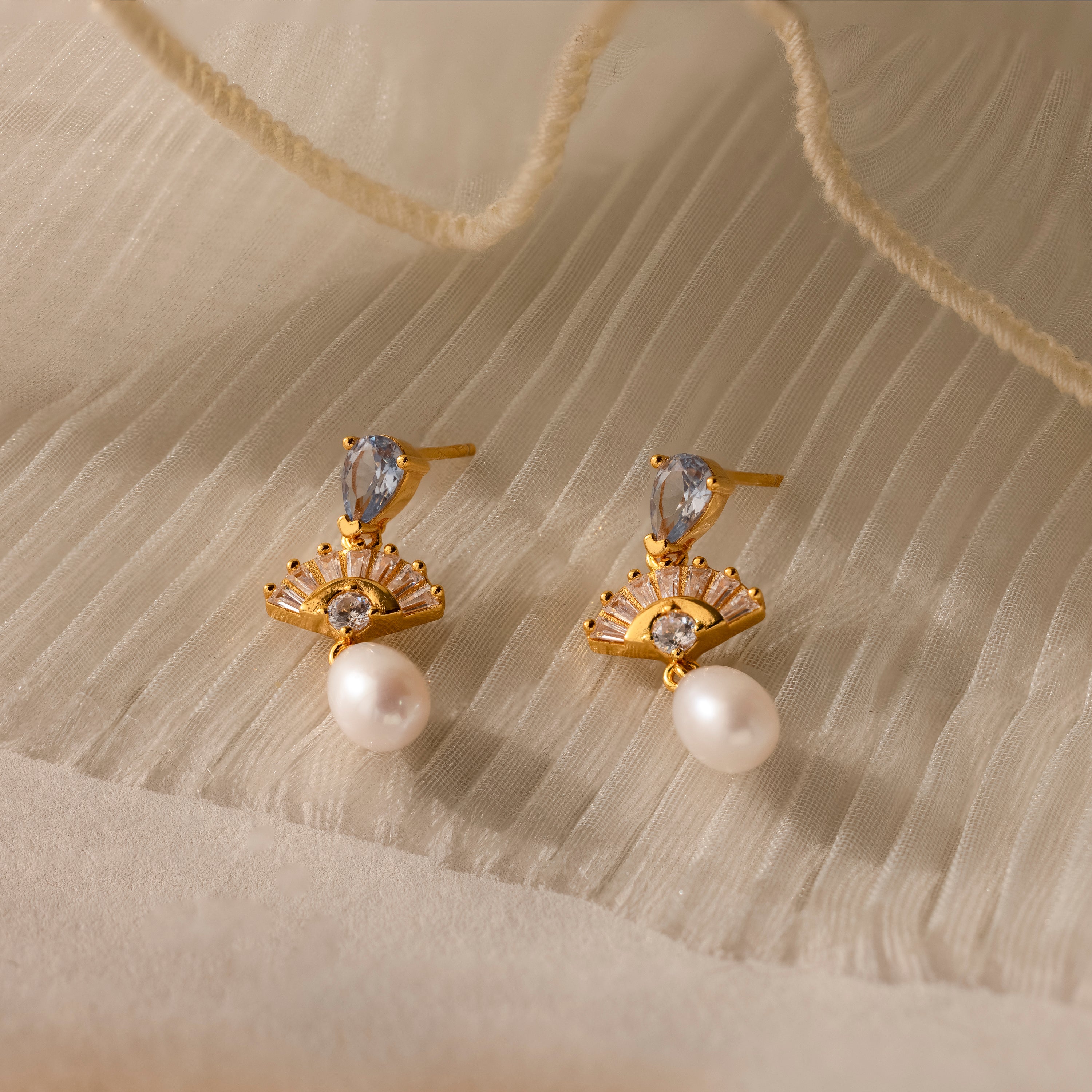 Aquamarine Pearl Drop Earrings in 18K Gold, styled on a textured cream fabric, feature clear stones and pearl drops—ideal wedding earrings for a touch of vintage glamour.
