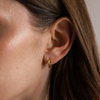 Close-up of a woman's ear with brown hair, wearing the Love Knot Huggies in 18K Gold—an elegant earring symbolizing lasting bonds.