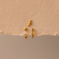 The Topaz Earring Trio Set features four small gold earrings with yellow gemstones, beautifully displayed on a torn piece of beige textured paper—perfect as a birthstone earring set.