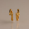 Floating Topaz Huggies: Gold hoop earrings with a curved design, each featuring a round yellow topaz at the center, shown on a neutral background.