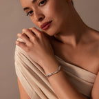 A woman in a beige draped top wears the Organic Wavy Cuff Bracelet in Silver, featuring sculpted curves, as she looks softly at the camera against a neutral background.