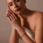 A woman in an off-shoulder top wears the Organic Mariner Chain Bracelet, resting her head on her clasped hands—a stylish touch of contemporary jewelry.
