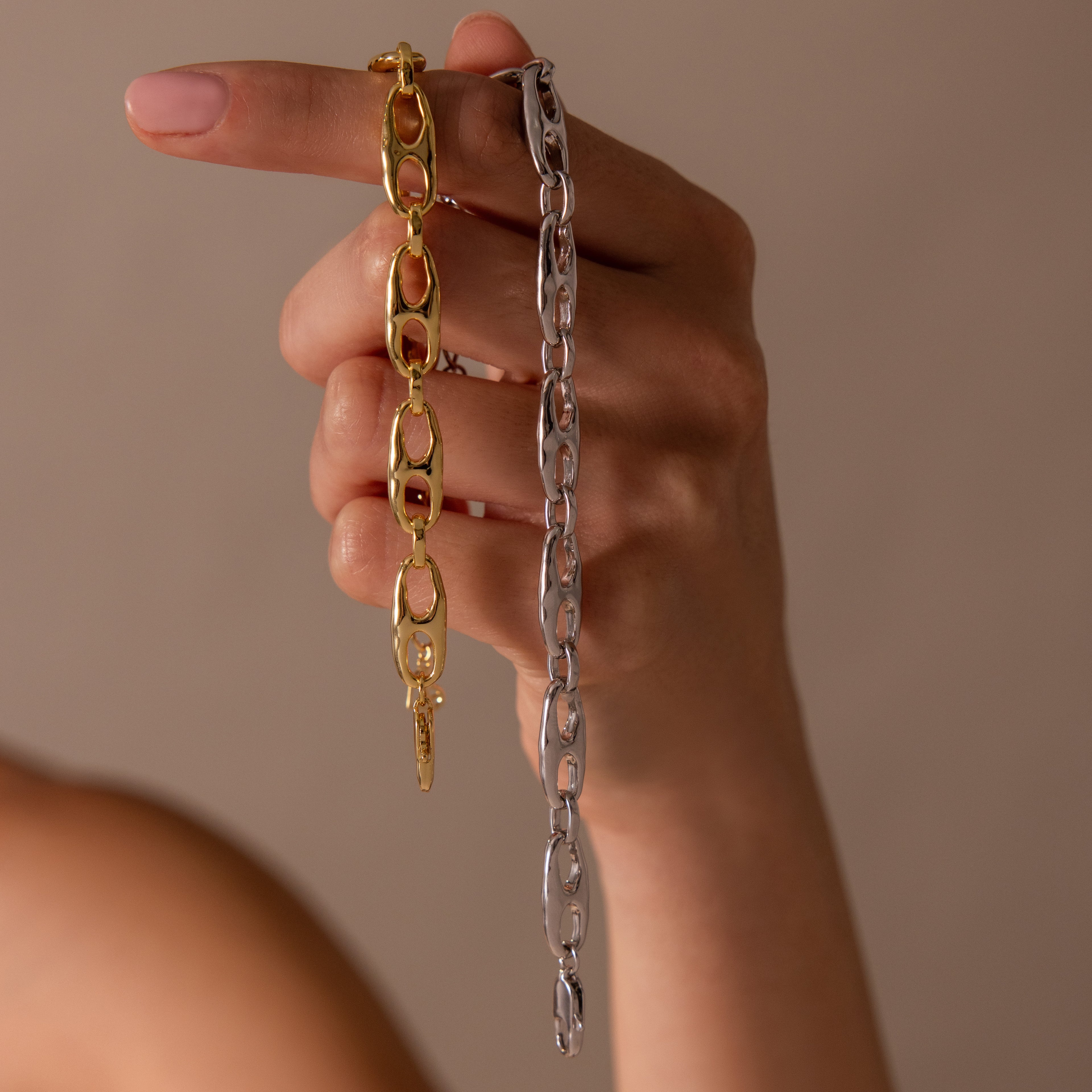 A hand displays the Organic Mariner Chain Bracelet, a contemporary piece with sculptural gold and silver links, draped elegantly over the fingers against a neutral background.