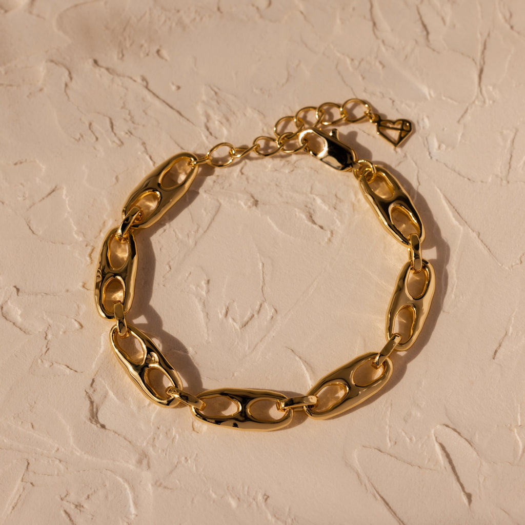 Timeless essential: the Organic Mariner Chain Bracelet in 18K Gold features elegant oval links, beautifully displayed on a textured beige surface.