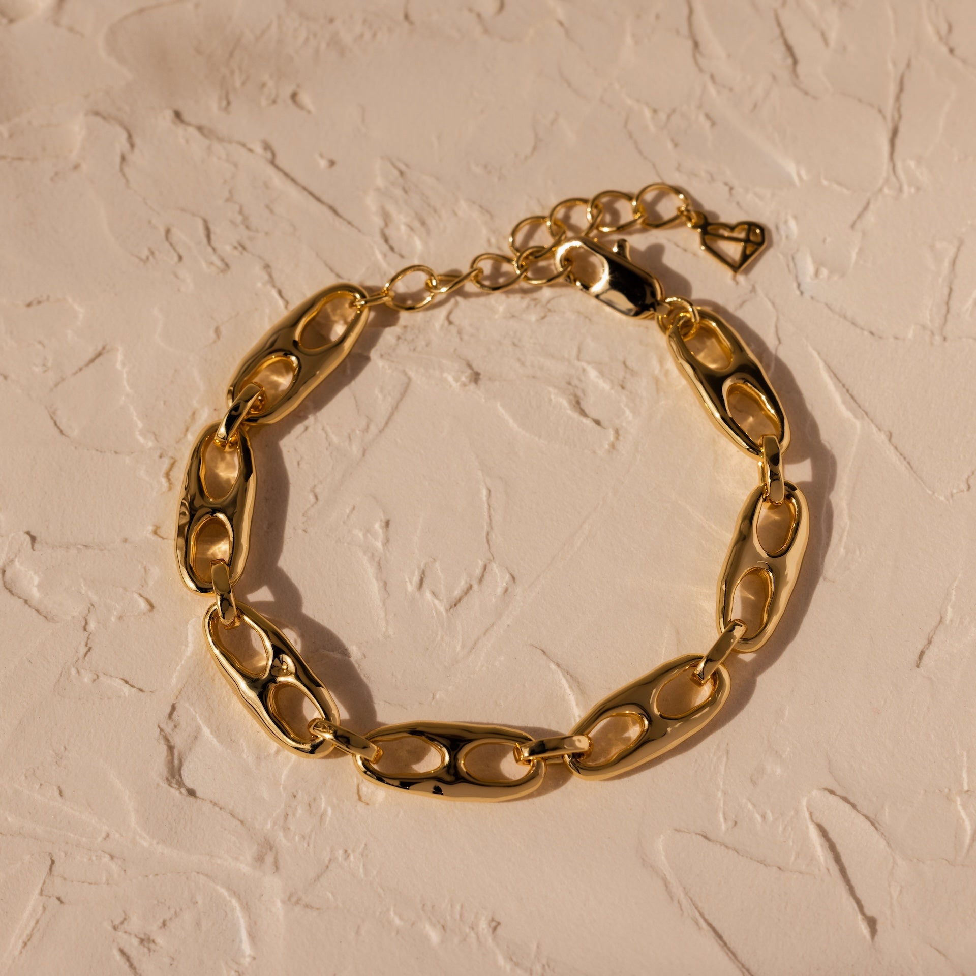 Timeless essential: the Organic Mariner Chain Bracelet in 18K Gold features elegant oval links, beautifully displayed on a textured beige surface.