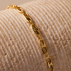 The Organic Mariner Chain Bracelet in 18K Gold, featuring sculptural oval links, is displayed on a textured beige surface—a timeless piece that effortlessly elevates any style.