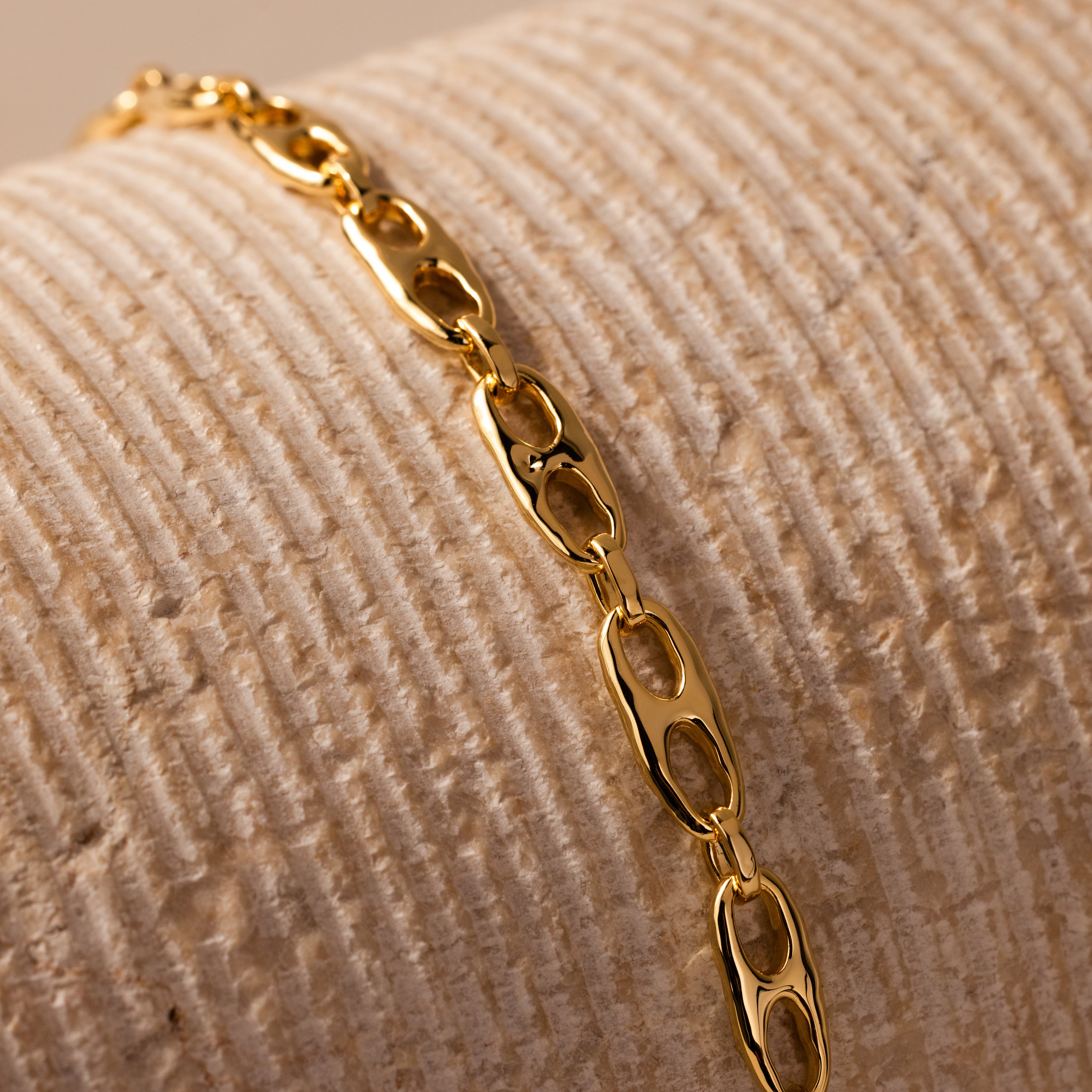 The Organic Mariner Chain Bracelet in 18K Gold, featuring sculptural oval links, is displayed on a textured beige surface—a timeless piece that effortlessly elevates any style.