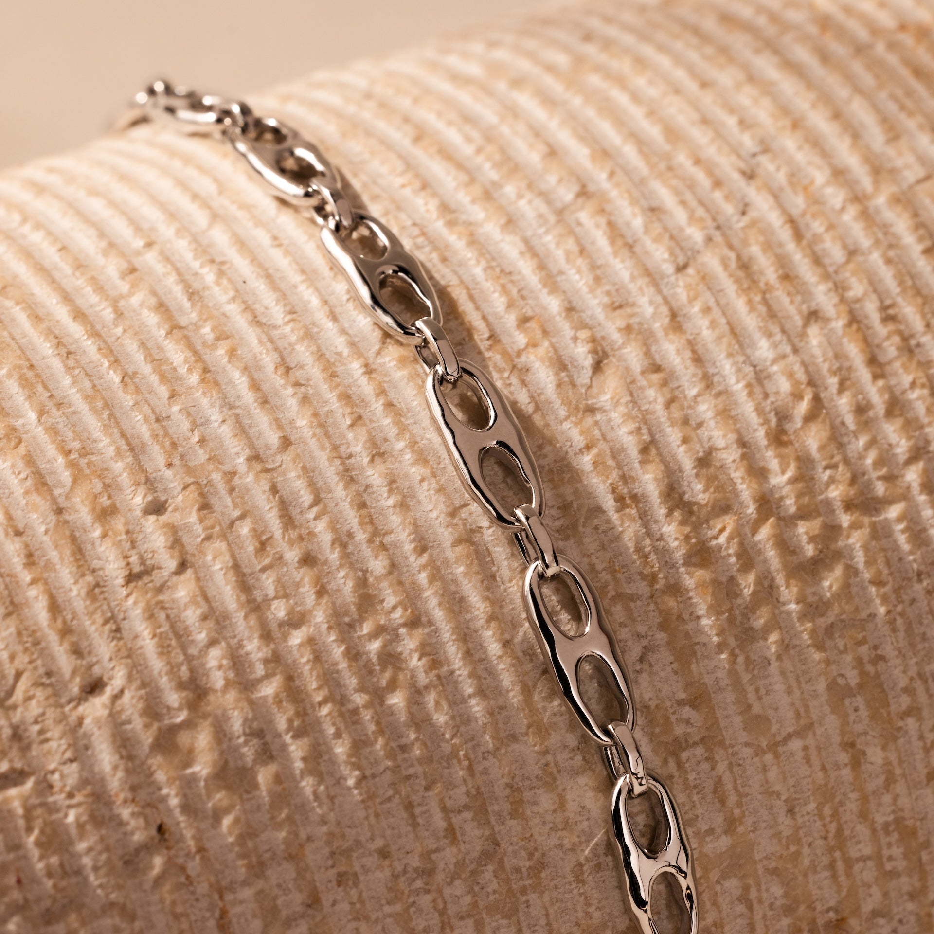 Displayed on a textured cream surface, the Organic Mariner Chain Bracelet in silver features sculptural oval links—an ideal pick for fans of modern, contemporary jewelry.