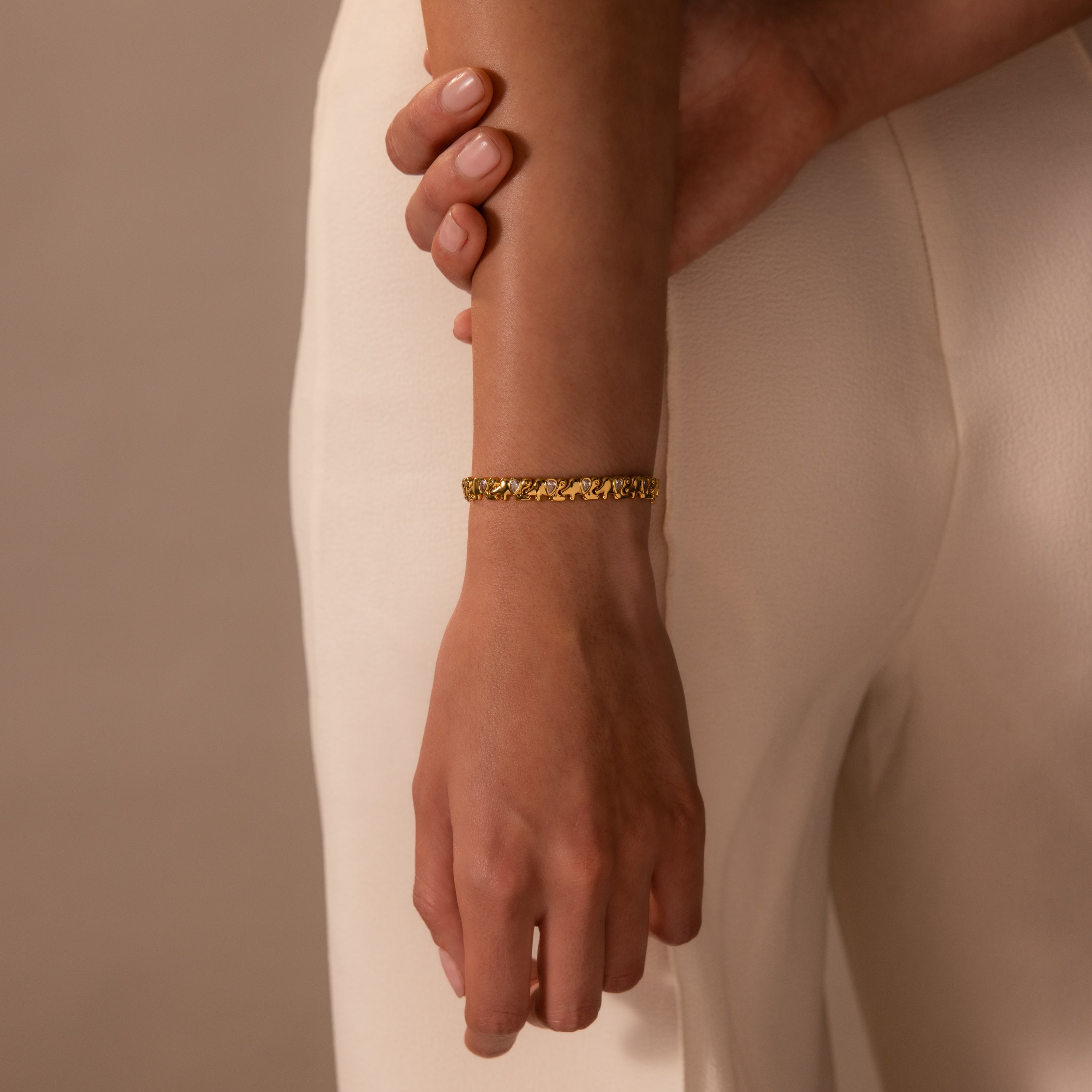A person wearing a Diamond Elephant Link Bracelet and cream-colored pants, with one hand gently holding their arm.