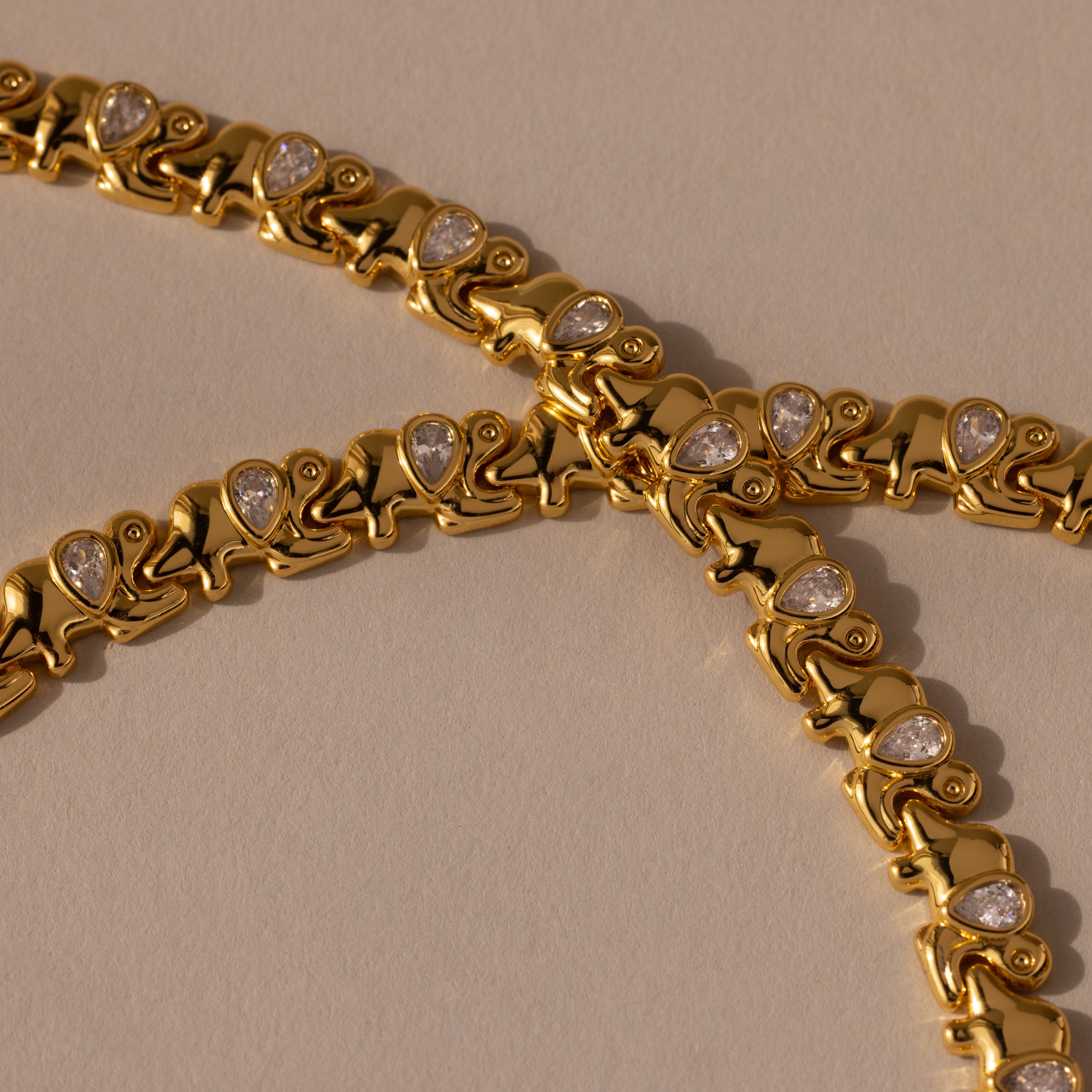 Gold bracelets with repeating chameleon motifs and teardrop crystals rest on a beige surface beside the Diamond Elephant Link Bracelet, creating an elegant, animal-inspired ensemble.