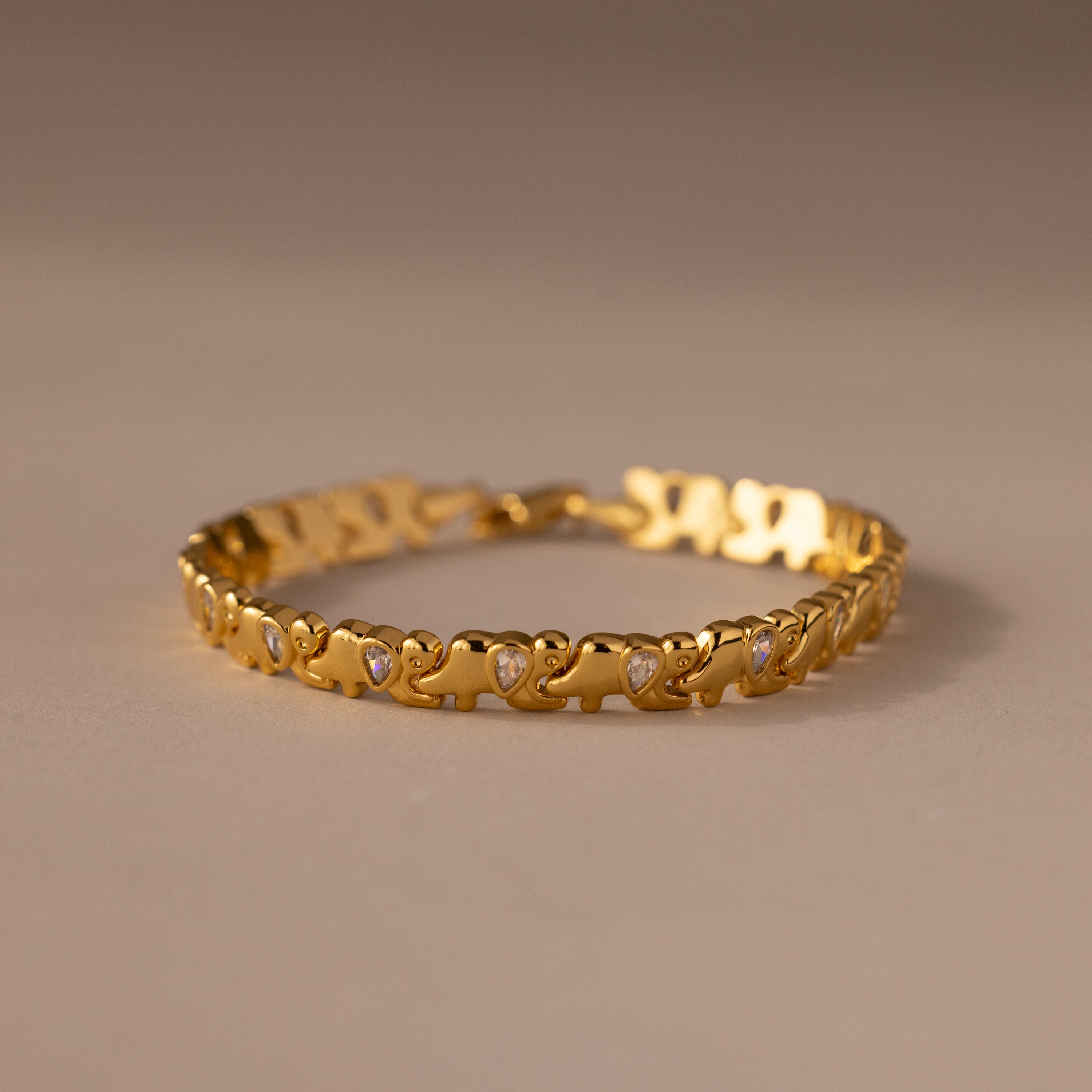 The Diamond Elephant Link Bracelet features a gold design with repeating heart patterns and small diamonds, elegantly displayed on a neutral surface.