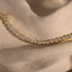 Elegant jewelry showcasing the Heart Tennis Bracelet in 18K Gold, adorned with heart-shaped diamonds and displayed on a textured beige stone surface.