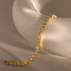The Heart Tennis Bracelet in 18K Gold, featuring teardrop-shaped diamonds, drapes elegantly over a soft matte white ceramic bowl—an exquisite piece of fine jewelry.