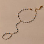 Ocean Beaded Hand Chain Bracelet in 18K Gold with blue beads, featuring a turquoise bracelet and ring linked by a delicate chain, showcased on a beige background.