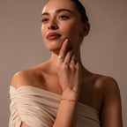 Woman in an off-the-shoulder beige top wears gold jewelry and the Ocean Beaded Hand Chain Bracelet, gazing thoughtfully to the side.