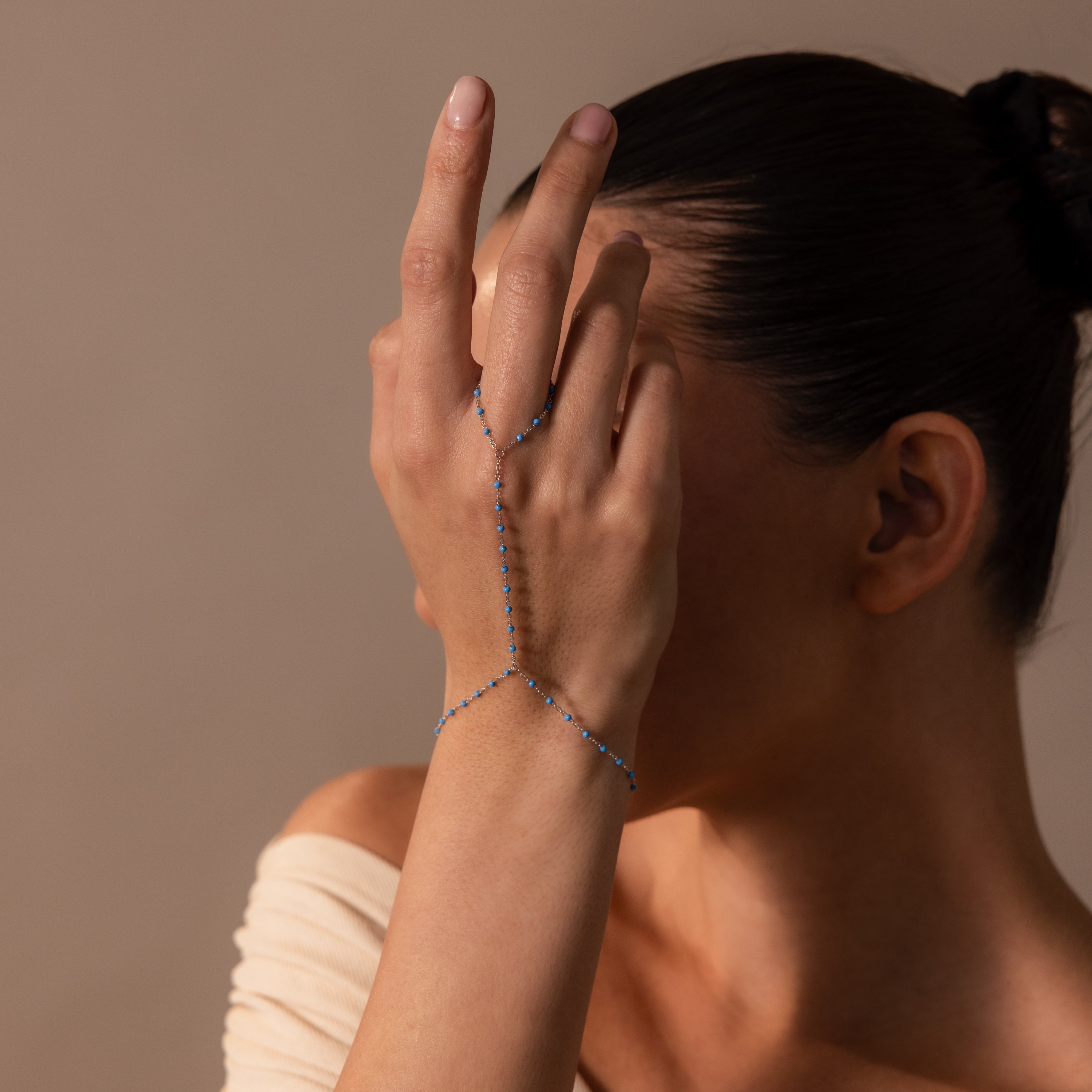 A woman covers her face with her hand, showcasing the Ocean Beaded Hand Chain Bracelet in Silver adorned with turquoise beads.