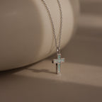 The Mother of Pearl Cross Necklace in Silver features an iridescent inlay pendant on a delicate chain, making it a timeless piece that shines beautifully against any neutral background.