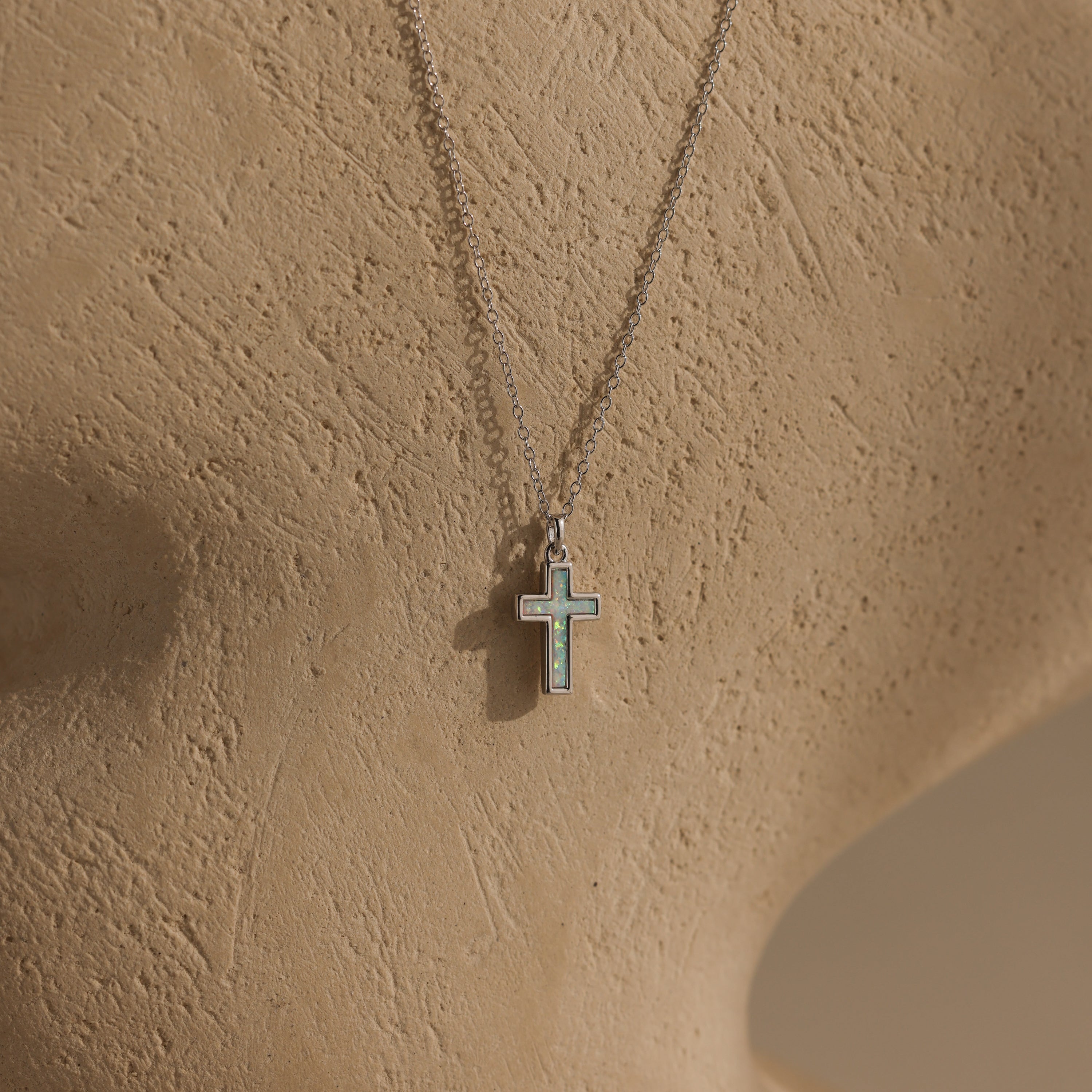 The Mother of Pearl Cross Necklace in Silver features an iridescent inlay pendant and is displayed on a textured beige mannequin bust—a timeless piece that brings elegance to any style.