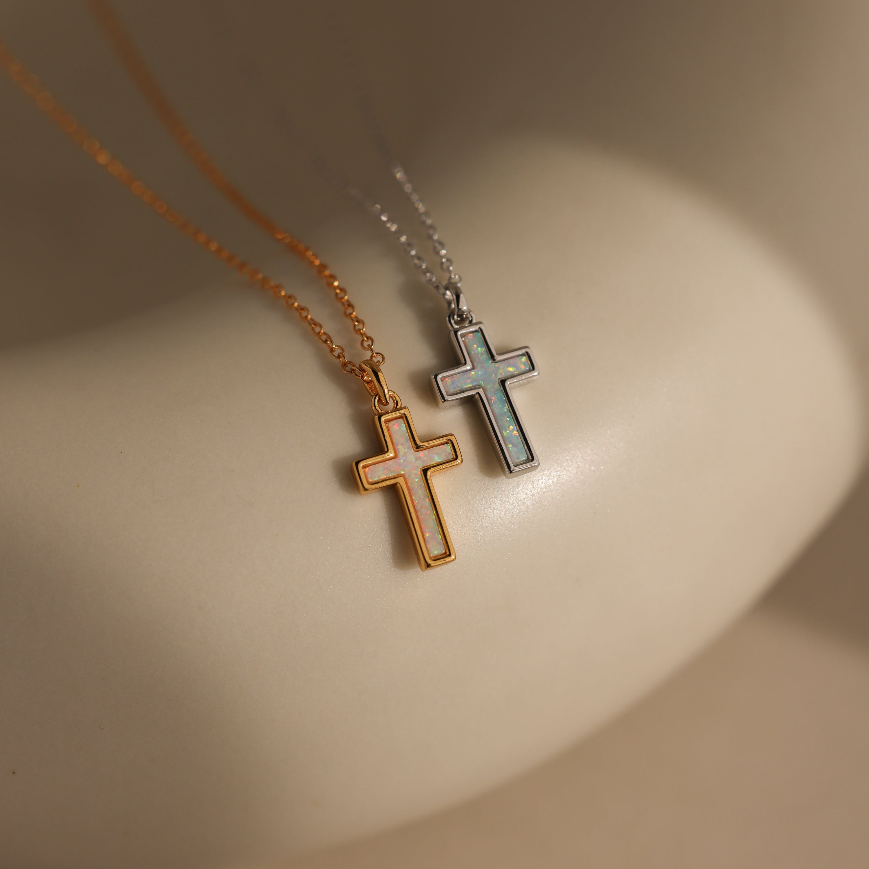 Two Mother of Pearl Cross Necklaces, one with a gold chain and one with a silver chain, featuring iridescent inlays, are displayed on a smooth, light surface—a stunning showcase of timeless jewelry.