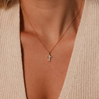The Mother of Pearl Cross Necklace in 18K Gold graces her neck, its shimmering inlay standing out against a cream knit V-neck top—a refined statement of timeless elegance.