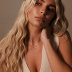 Woman with long wavy blonde hair wears a cream sleeveless top and the Mother of Pearl Cross Necklace in Silver, its iridescent inlay catching the light as she looks to the side.